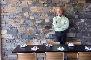 restaurant owner leaning against a stone wall beside the table