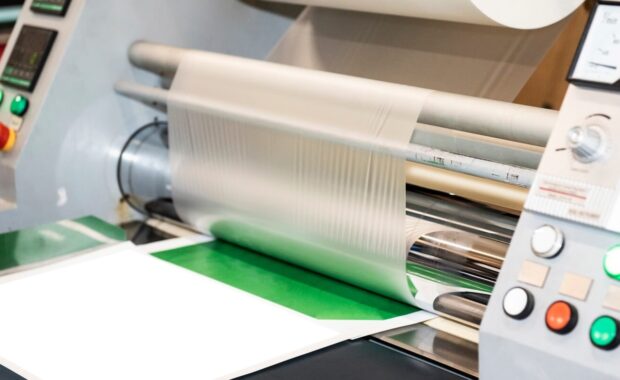 industrial laminator applies the film to the paper in the production room of the printing house