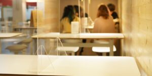 clear acrylic or plastic divider, barrier or partition on empty table in food court as part of safety protection for customers in background