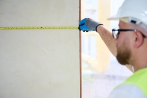 construction worker measuring a wall in the new house with roller tape