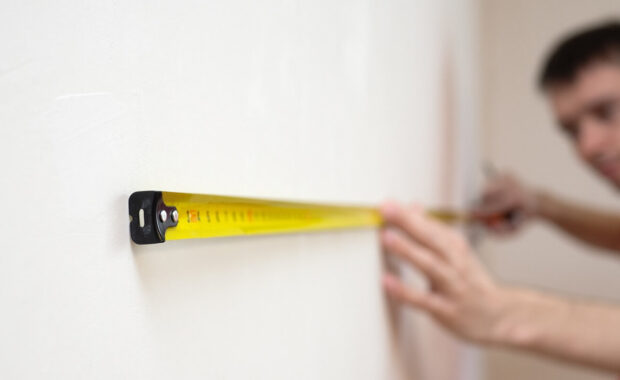 man repair measures the white wall of the with a tape measure and before wallpapering. renovation apartment